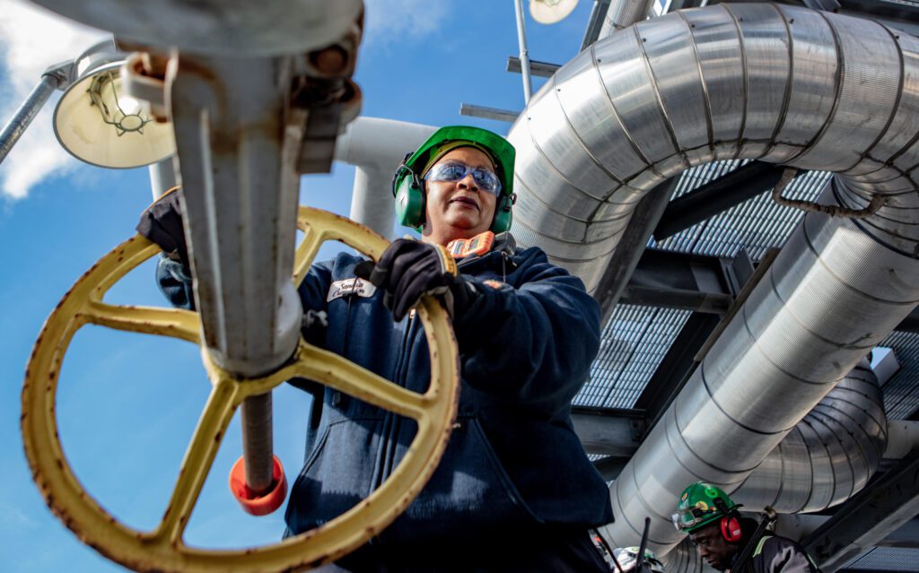 Refinery employee standing with their hands on a wheel at a refinery.