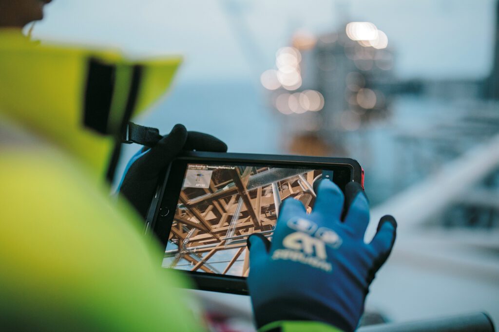 Digitalisation on Johan Sverdrup, close up of an engineer with a gloved hand using a handheld device.
